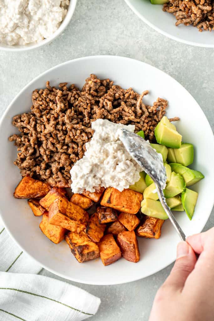 Adding a scoop of dairy free cottage cheese to the bowls.
