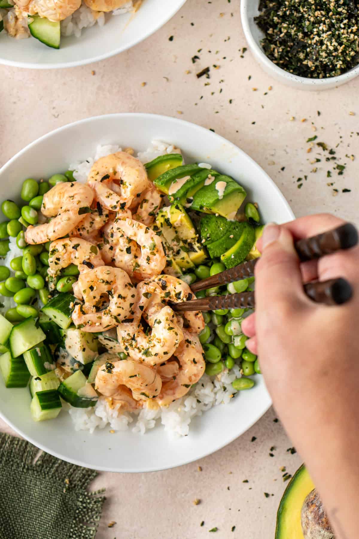 A hand with chopsticks taking a bite of creamy mayo prawns from the rice bowls.