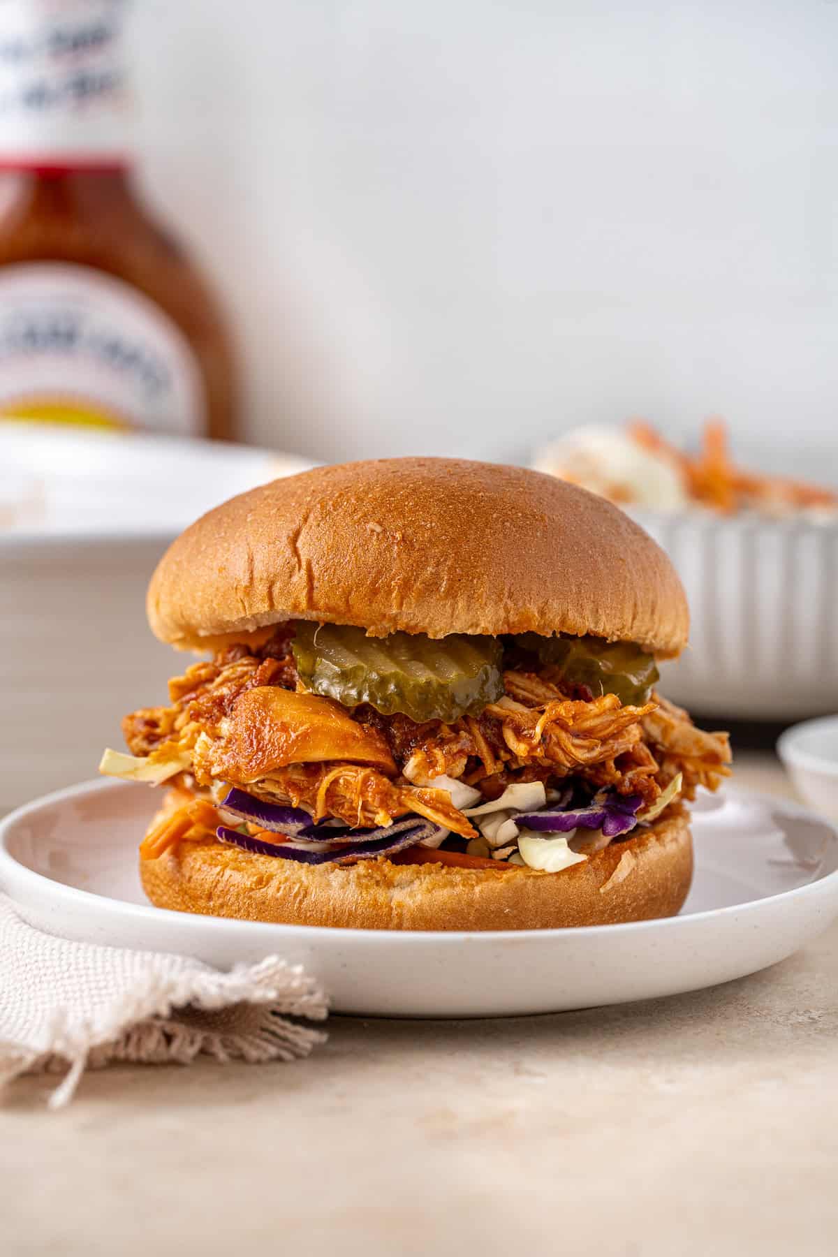 Slow cooker BBQ chicken on a bun with coleslaw and pickles.