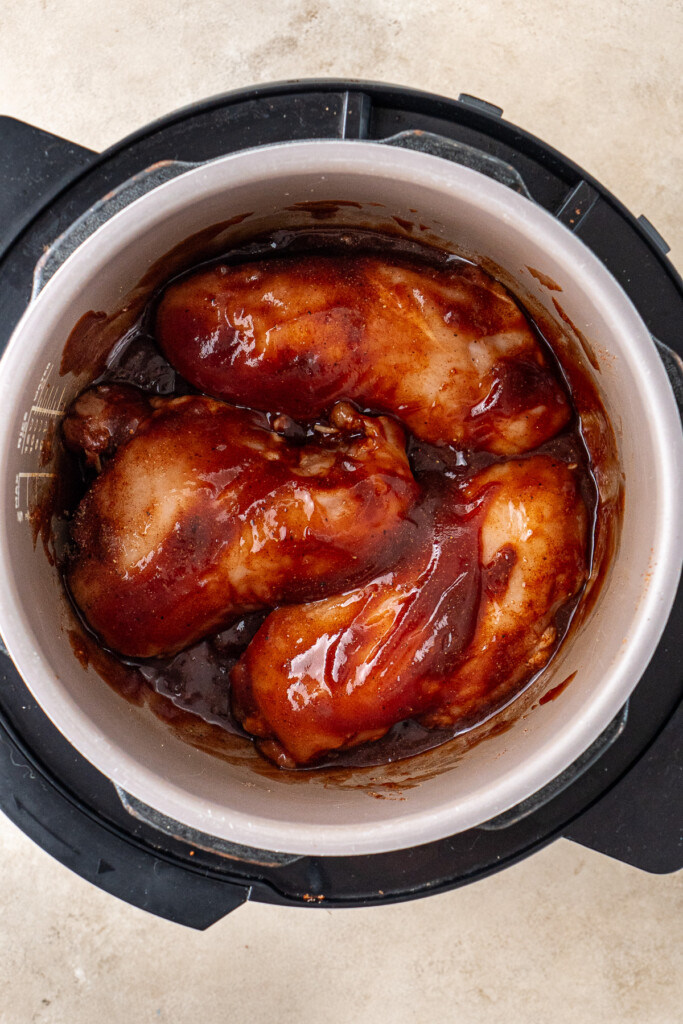 The raw chicken in the slow cooker with BBQ sauce.