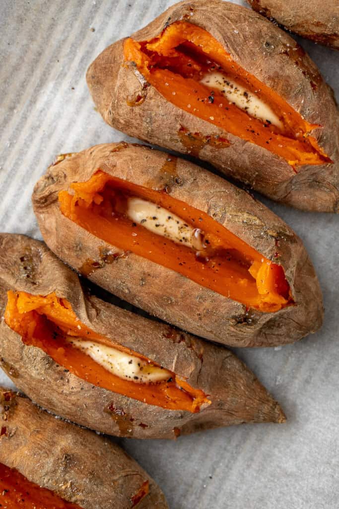 Splitting the sweet potatoes and seasoning with dairy free butter and salt and pepper.