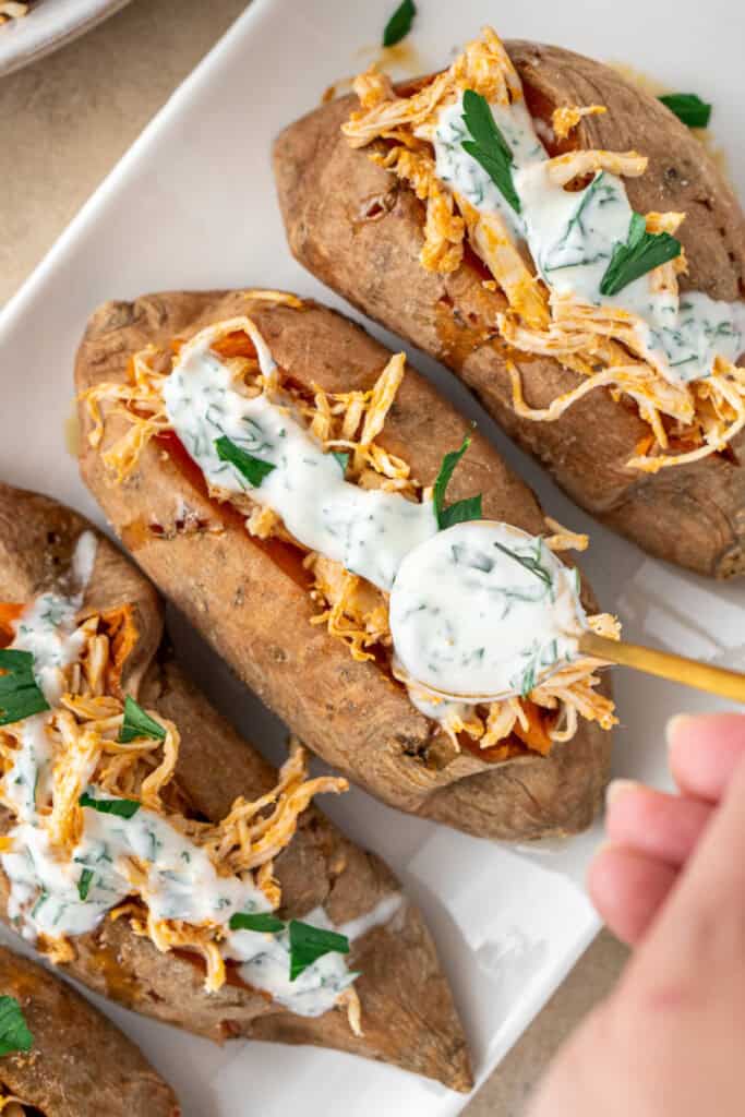 Drizzling ranch dressing over stuffed sweet potatoes.