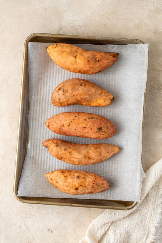 Whole sweet potatoes on a baking tray.