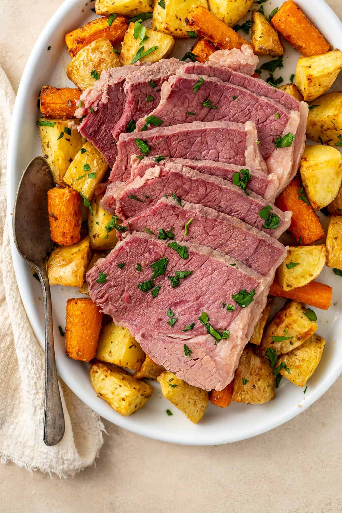 Sliced slow cooked corned beef served on a plate of roasted vegetables.