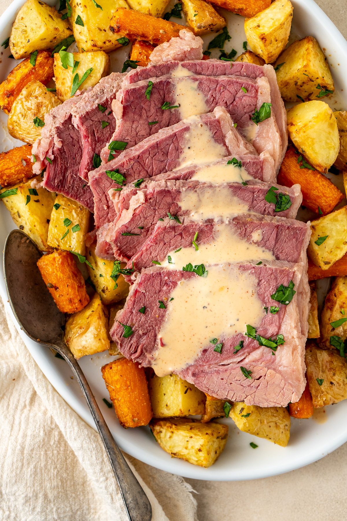 Sliced corned silverside on a plate with roasted potatoes and carrots and a drizzle of white sauce.