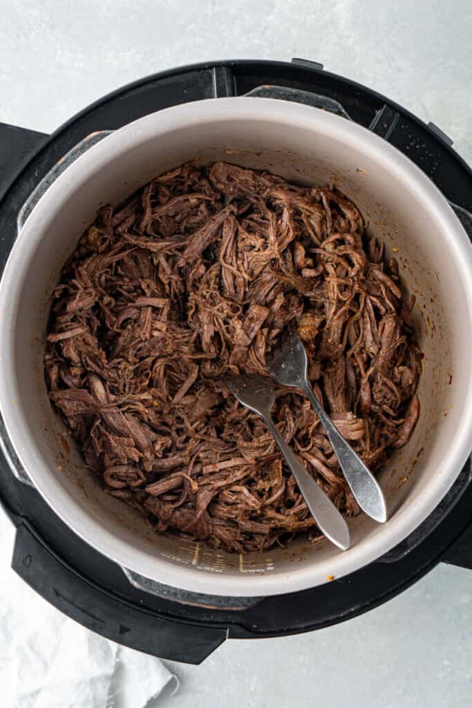 Two forks shredding the beef in the slow cooker.