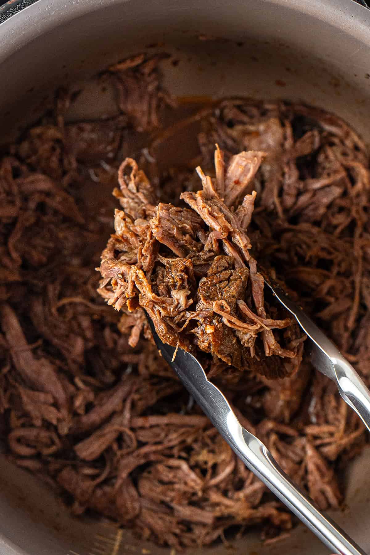 Close up of tongs holding pulled mexican beef.