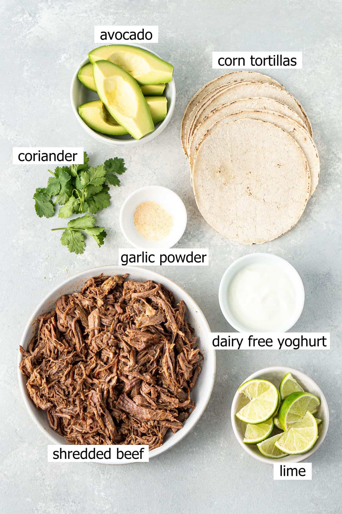 All ingredients needed for shredded beef tacos laid out in bowls.