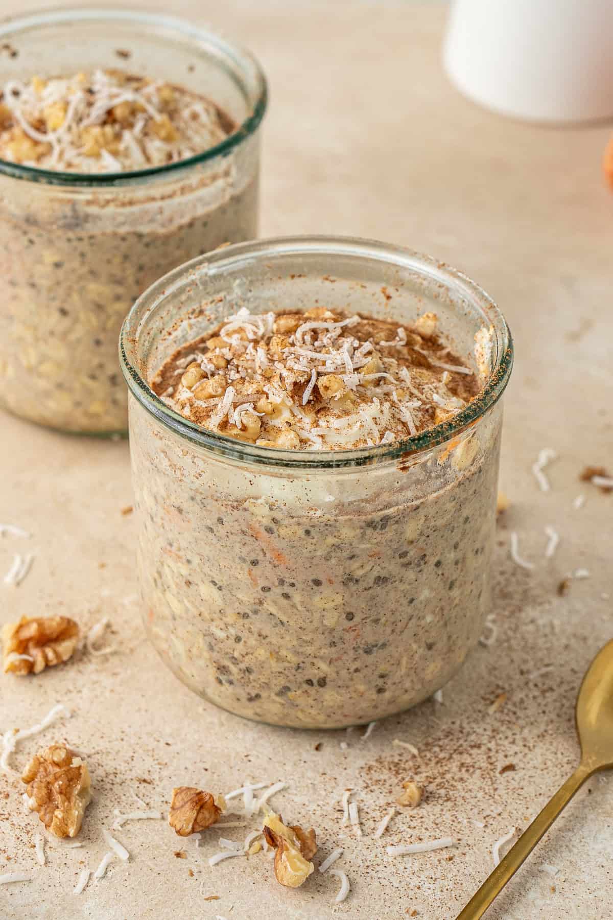 Carrot cake overnight oats with yoghurt, walnuts and shredded coconut in jars ready to eat. 
