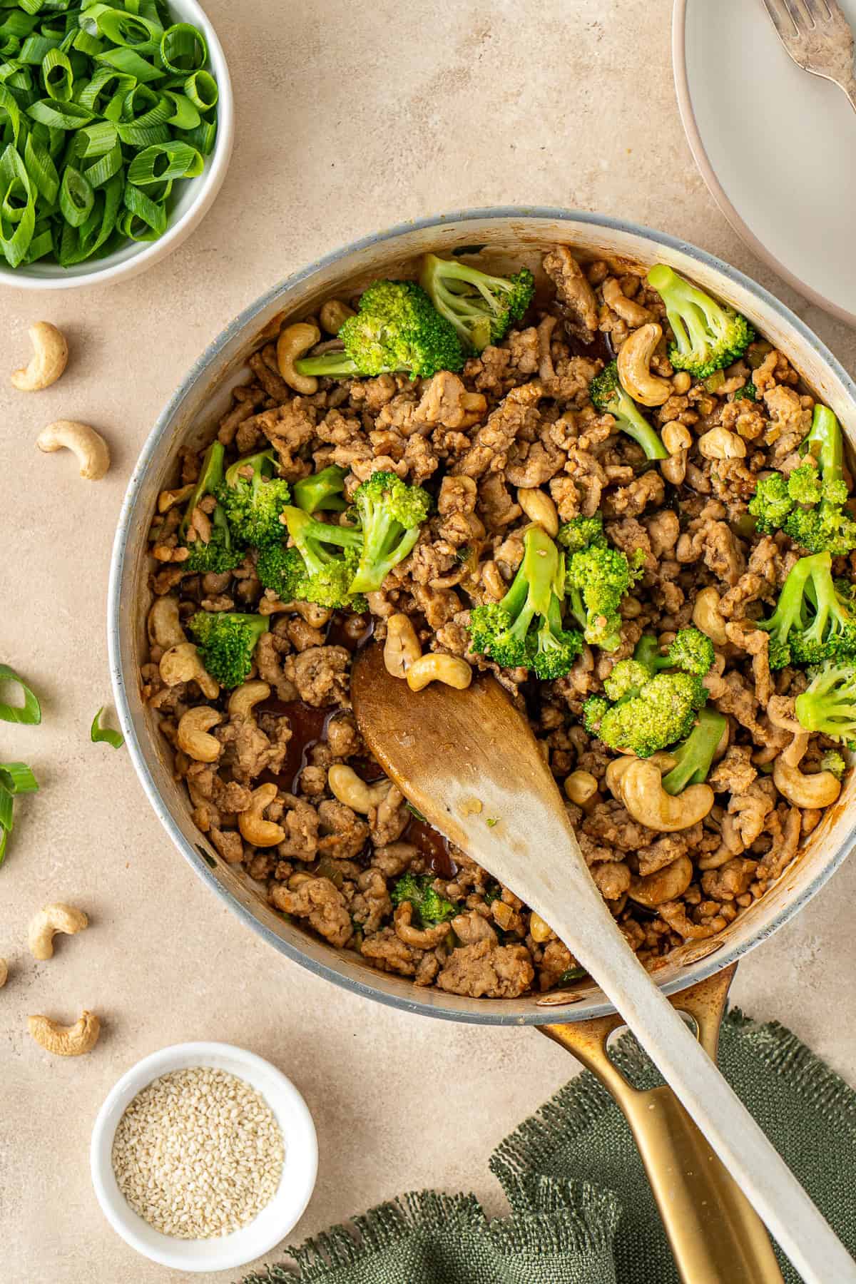 Close up of the cashew chicken and broccoli in a frying pan with a wooden spoon.