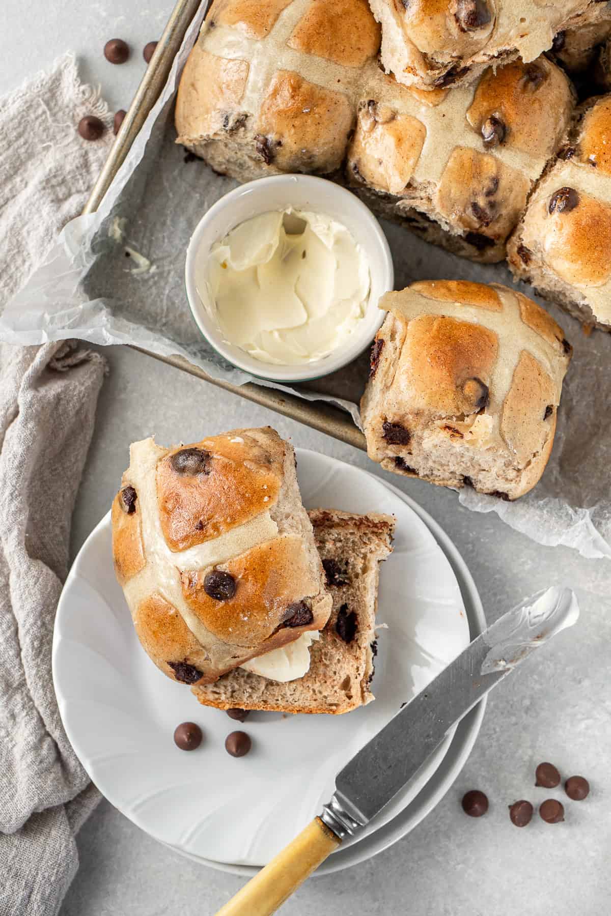 A choc chip hot cross bun split on a plate with dairy free butter.