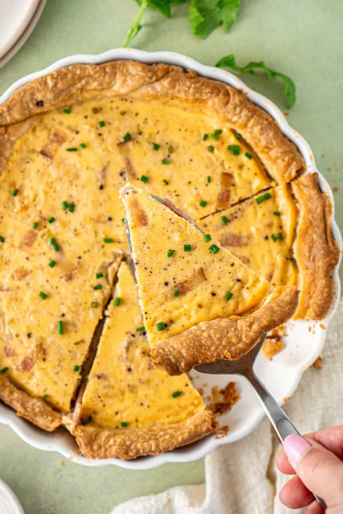 A hand serving out a slice of cooked quiche.