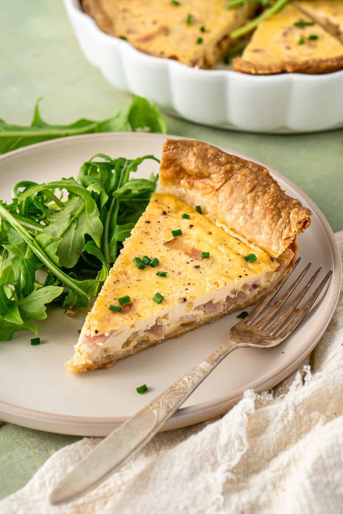 A slice of dairy free quiche on a plate with salad and a fork.
