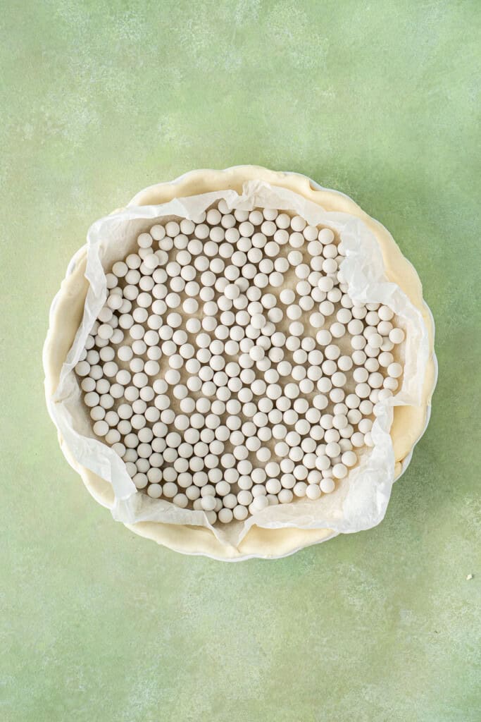 The pie crust with baking paper and pie weights.