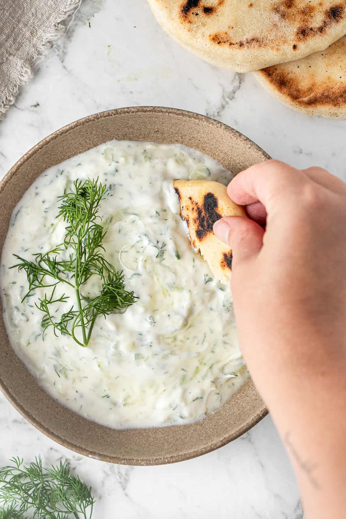 A hand dipping a piece of pita bread into the tzatziki. 