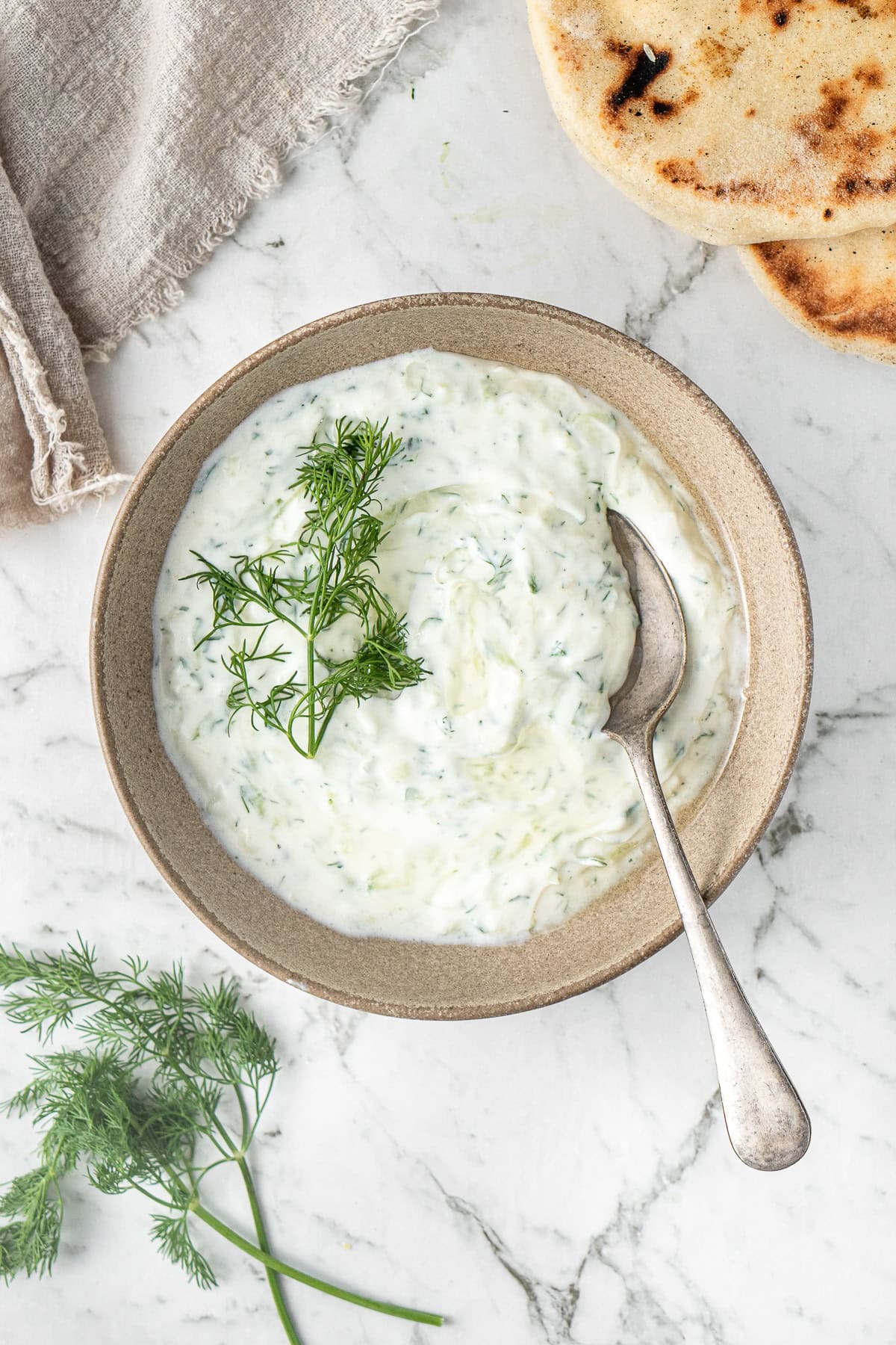 The dairy free tzatziki served in a bowl with a spoon and pita bread on the side.