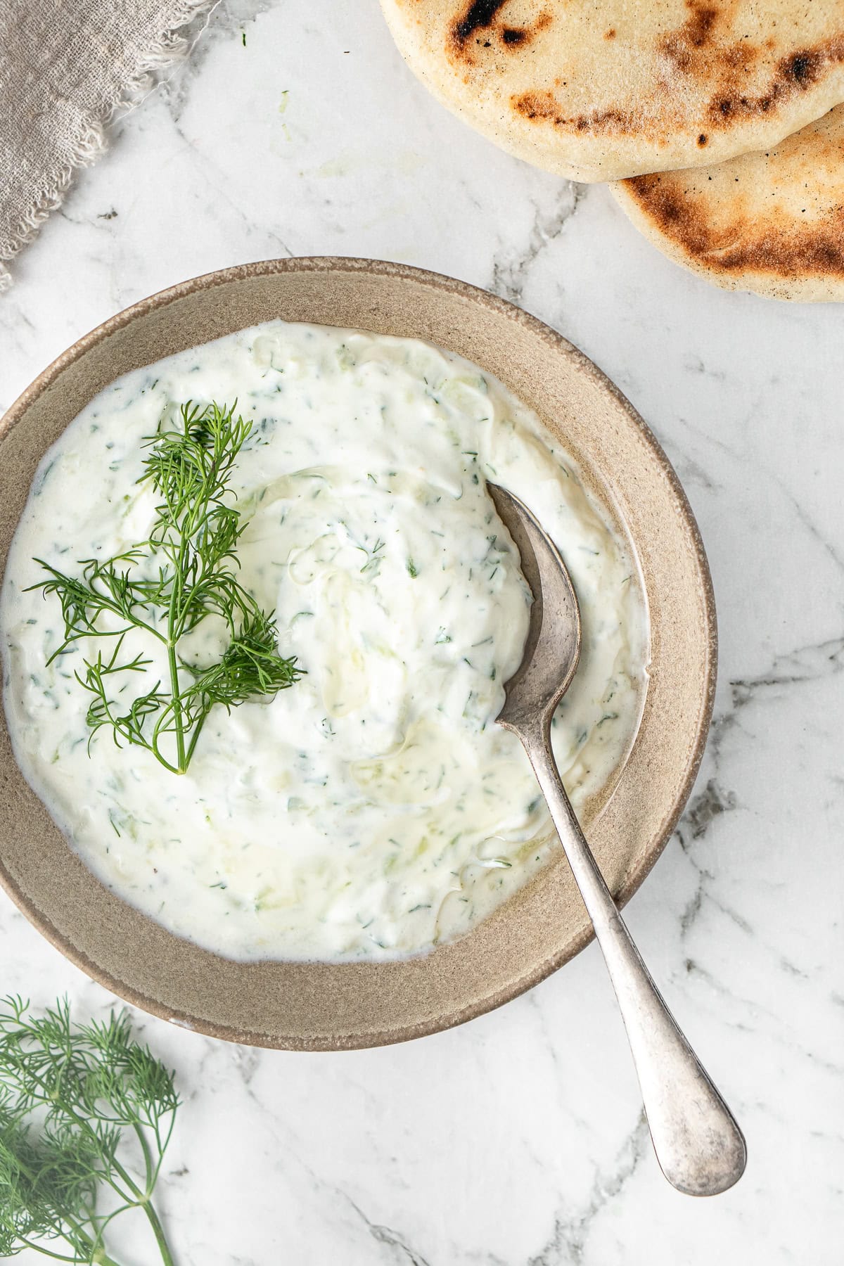Close up of the dairy free tzatziki served in a bowl with a spoon and pita bread on the side.