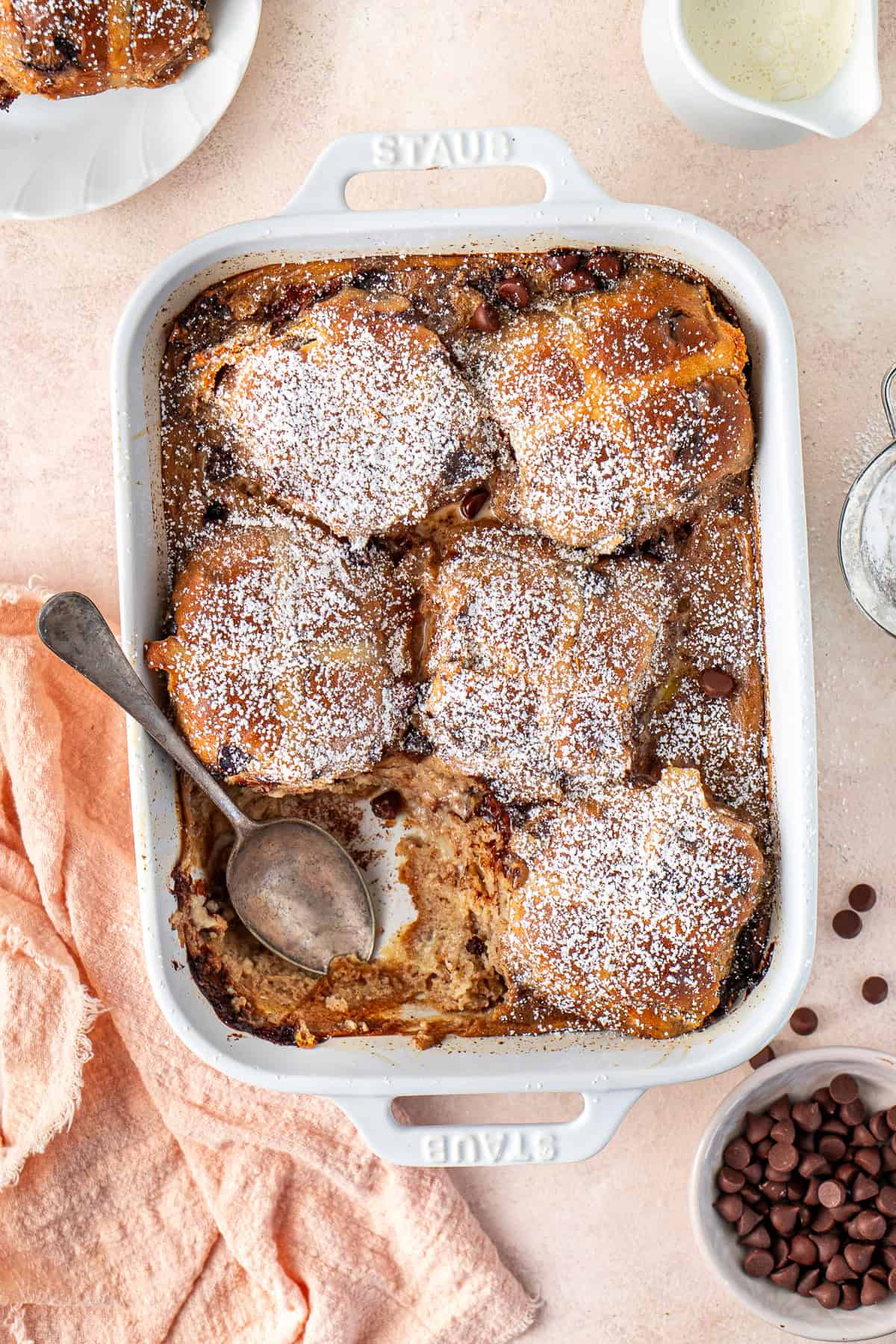 The dairy free hot cross bun bread and butter pudding in a rectangular baking dish with a serving spoon.