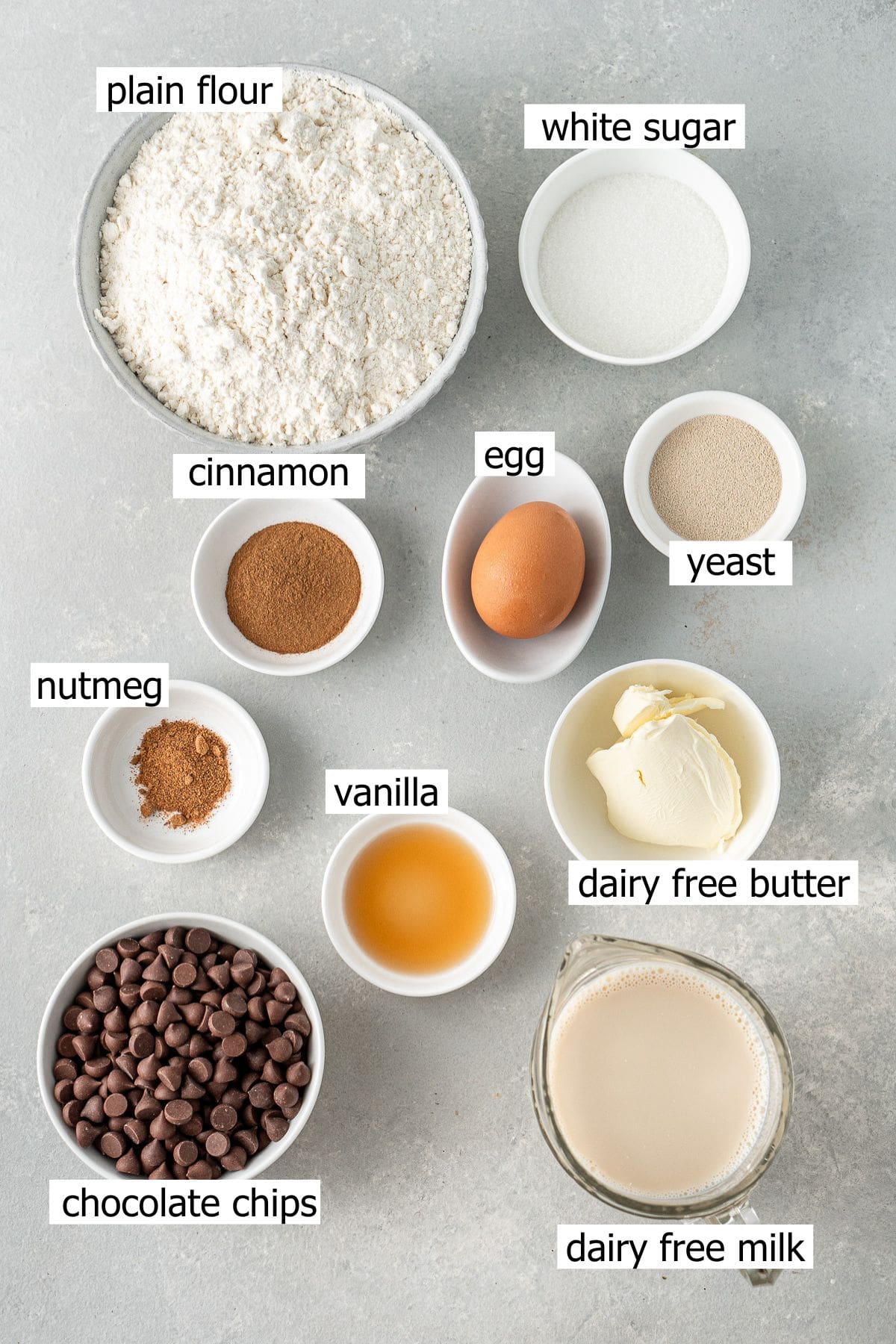 All ingredients needed to make choc chip hot cross buns laid out in small bowls.