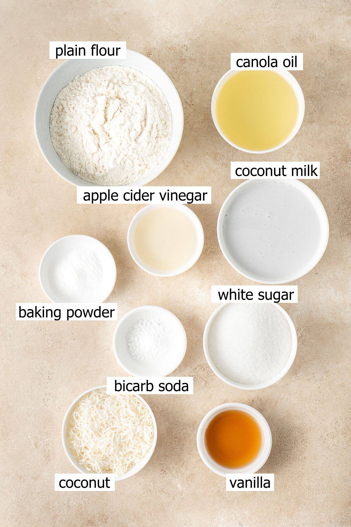 All ingredients needed to make vegan coconut cupcakes laid out in bowls.