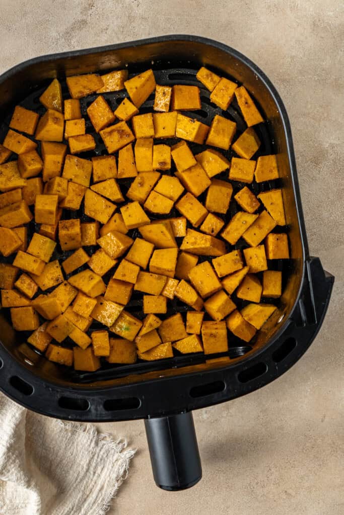 The pumpkin cubes in a single layer in the air fryer basket.