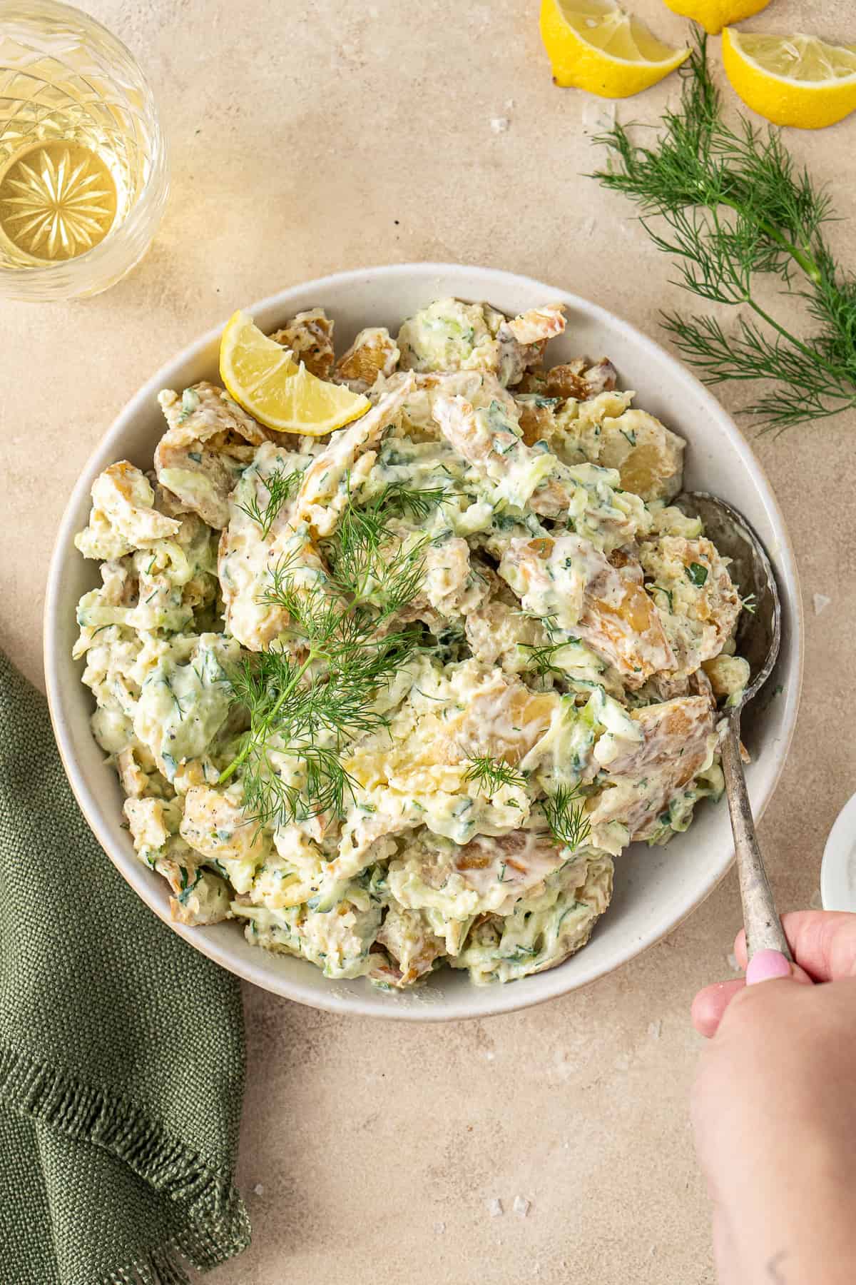 A spoon in a bowl of crispy smashed potato salad with dill and lemon.