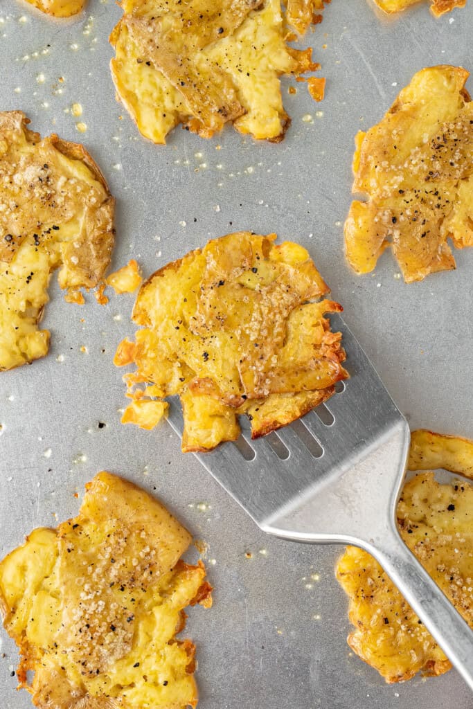 A spatula picking up a smashed potato off the tray.