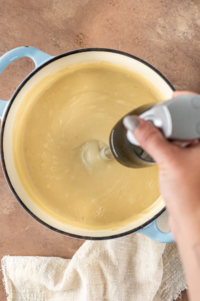 Using a stick blender to blend the potato soup in the pot.
