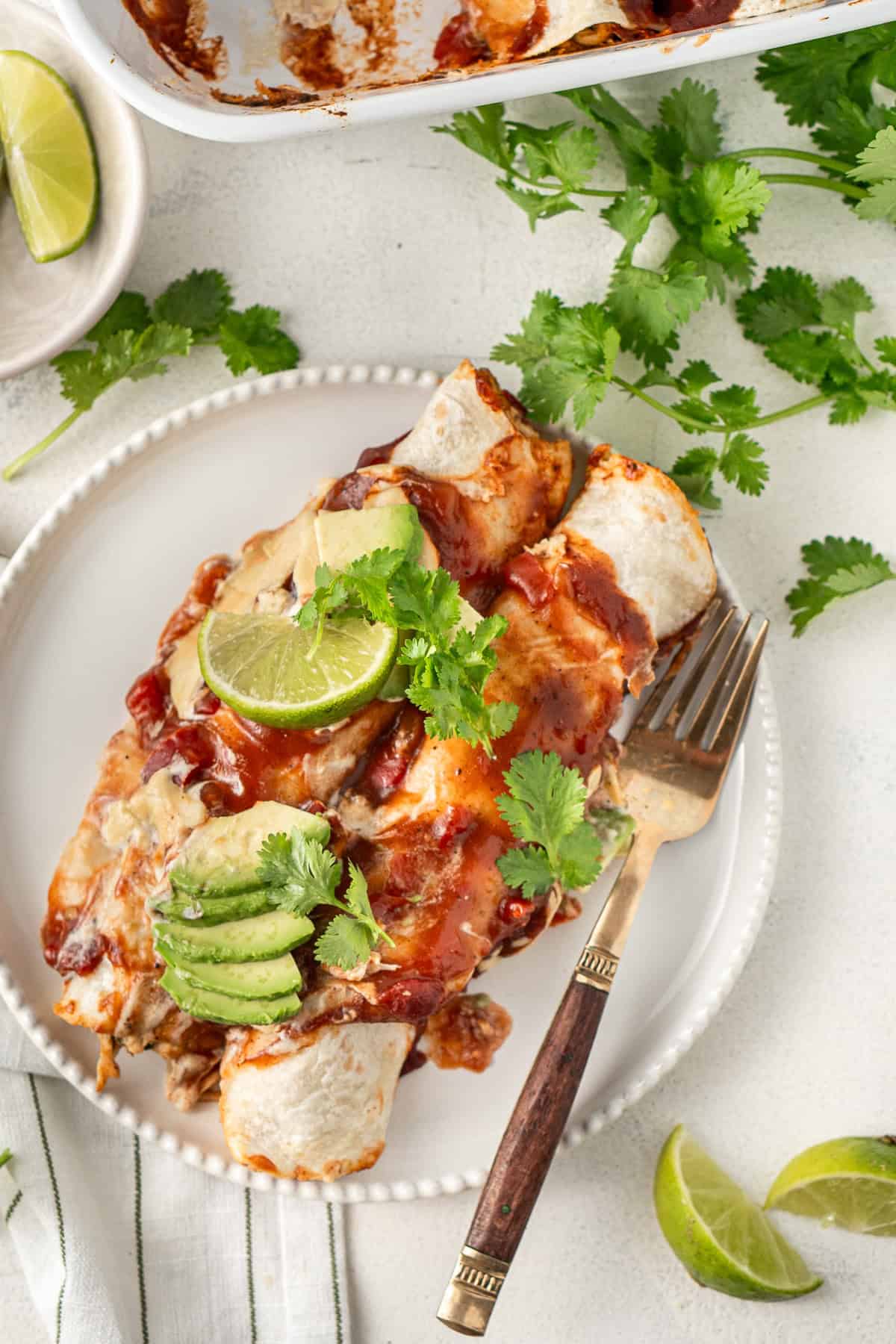 Two dairy free chicken enchiladas on a plate with coriander.