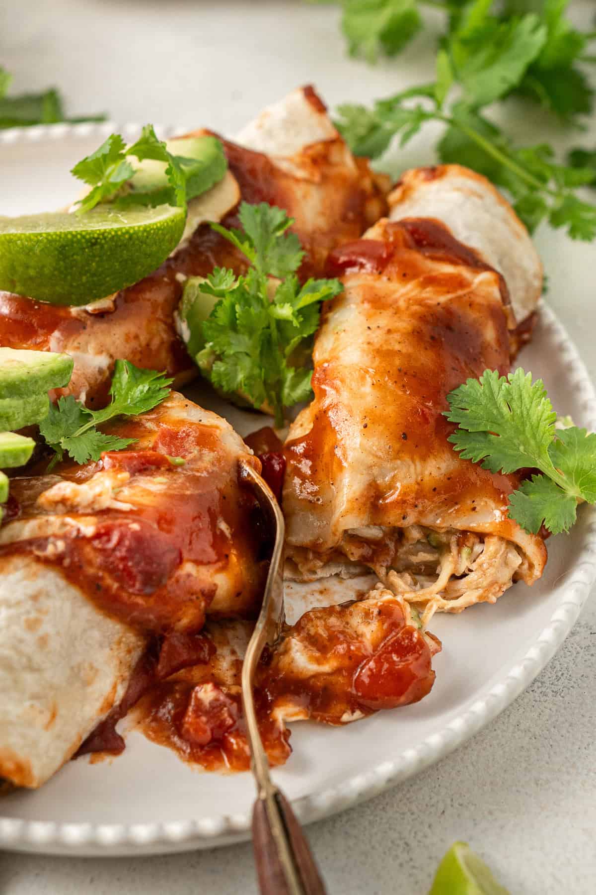 Close up of dairy free enchiladas on a plate with a fork breaking one in half to reveal the filling.
