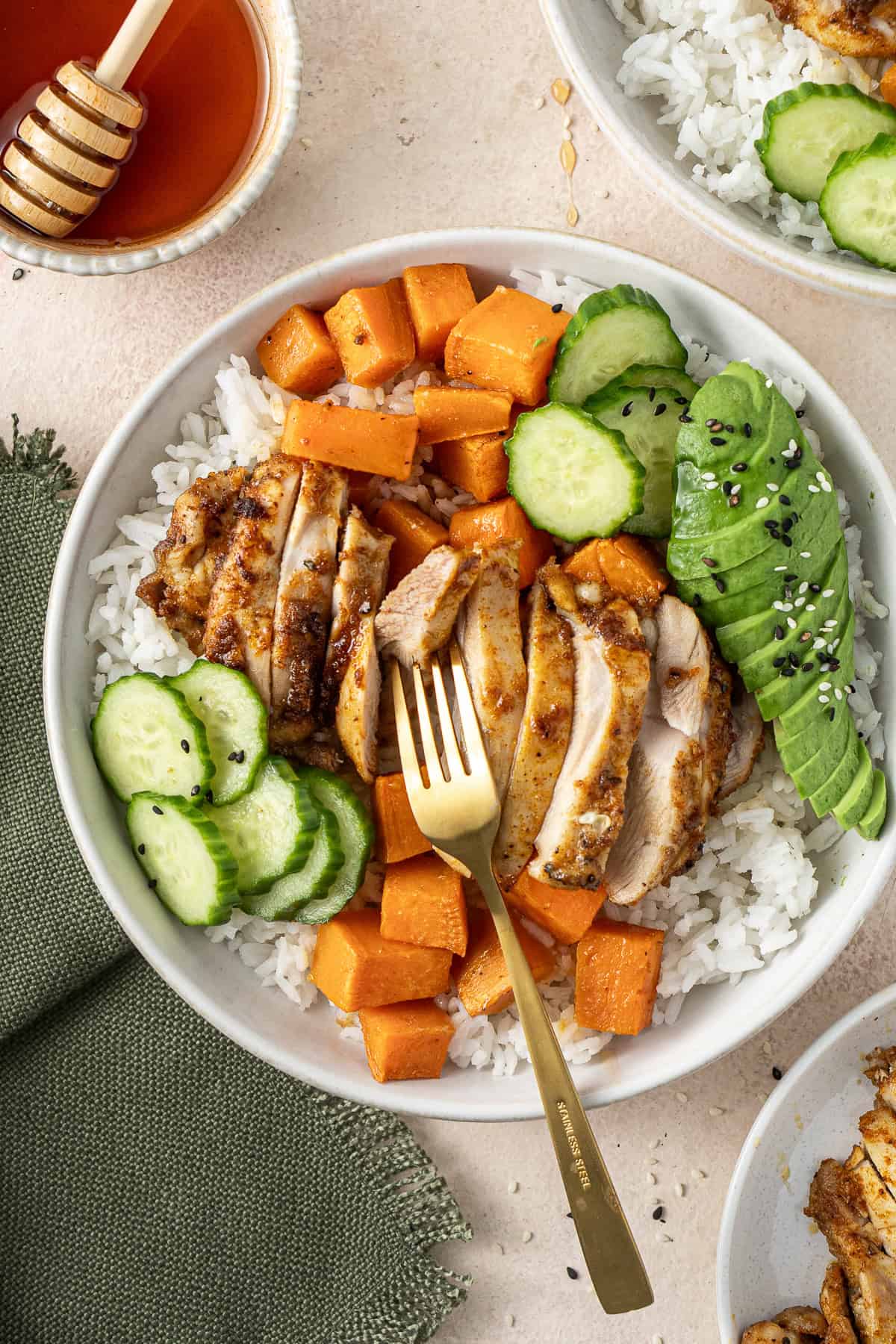 A fork in a bowl of chicken and sweet potato over rice with cucumber and avocado. 