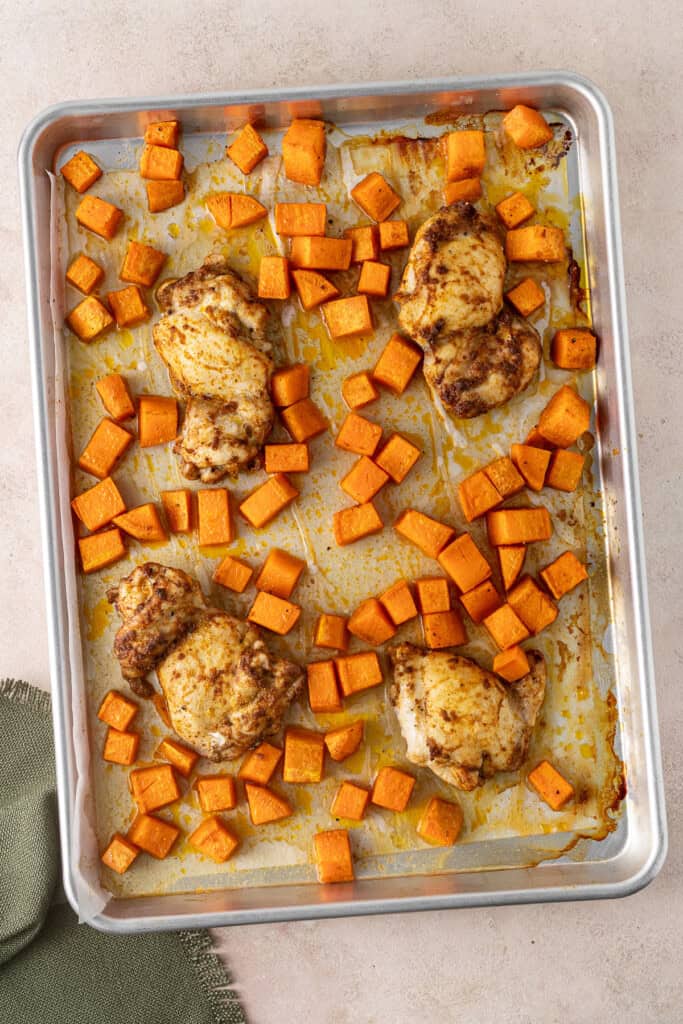 The cooked chicken thighs and sweet potato on a baking tray.