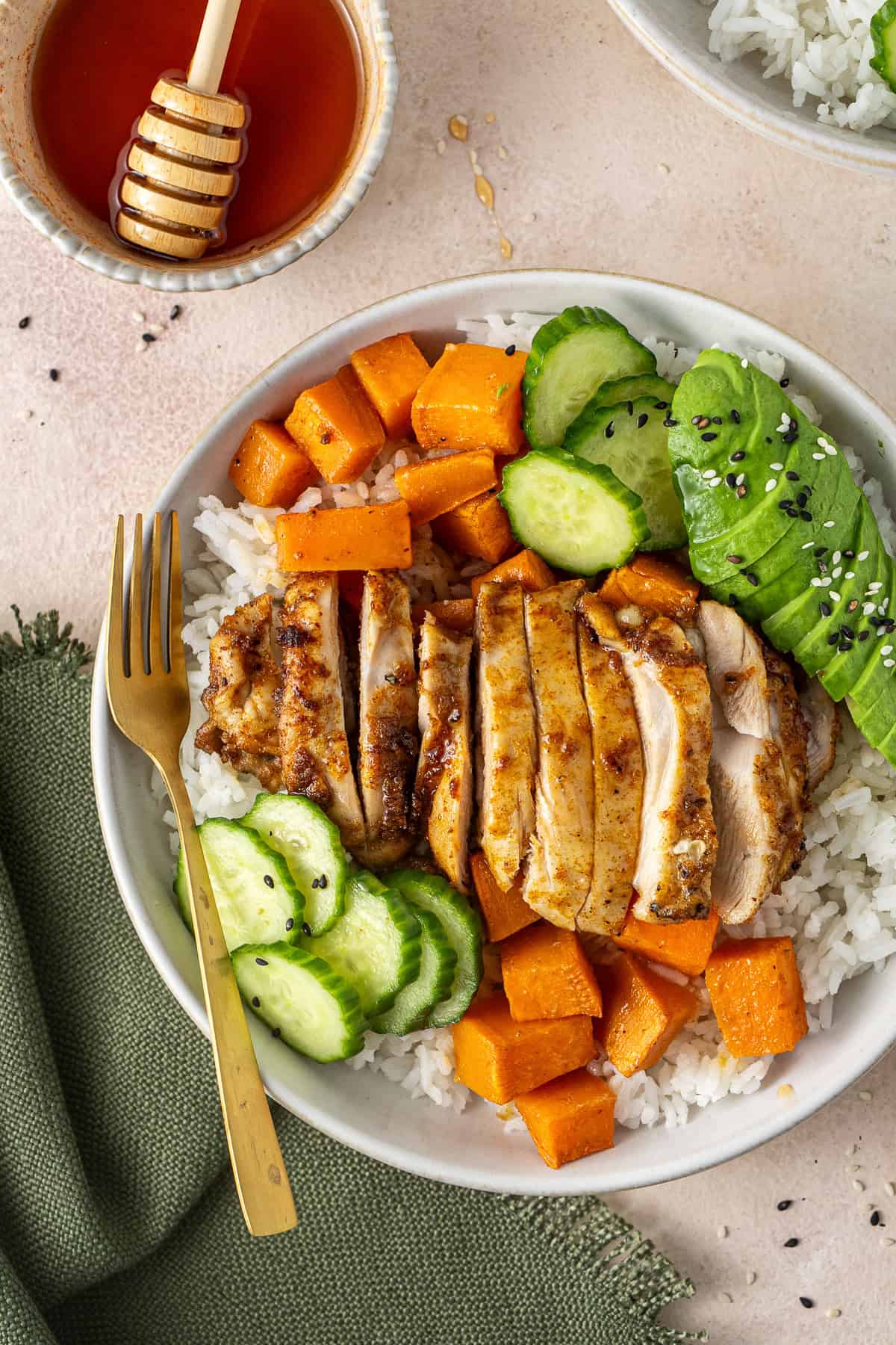 Close up of sliced chicken, sweet potato and cucumber with avocado and rice.