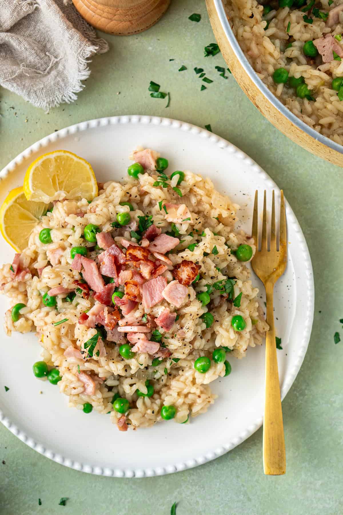Close up of the plated pea and bacon risotto with a form and lemon wedges.