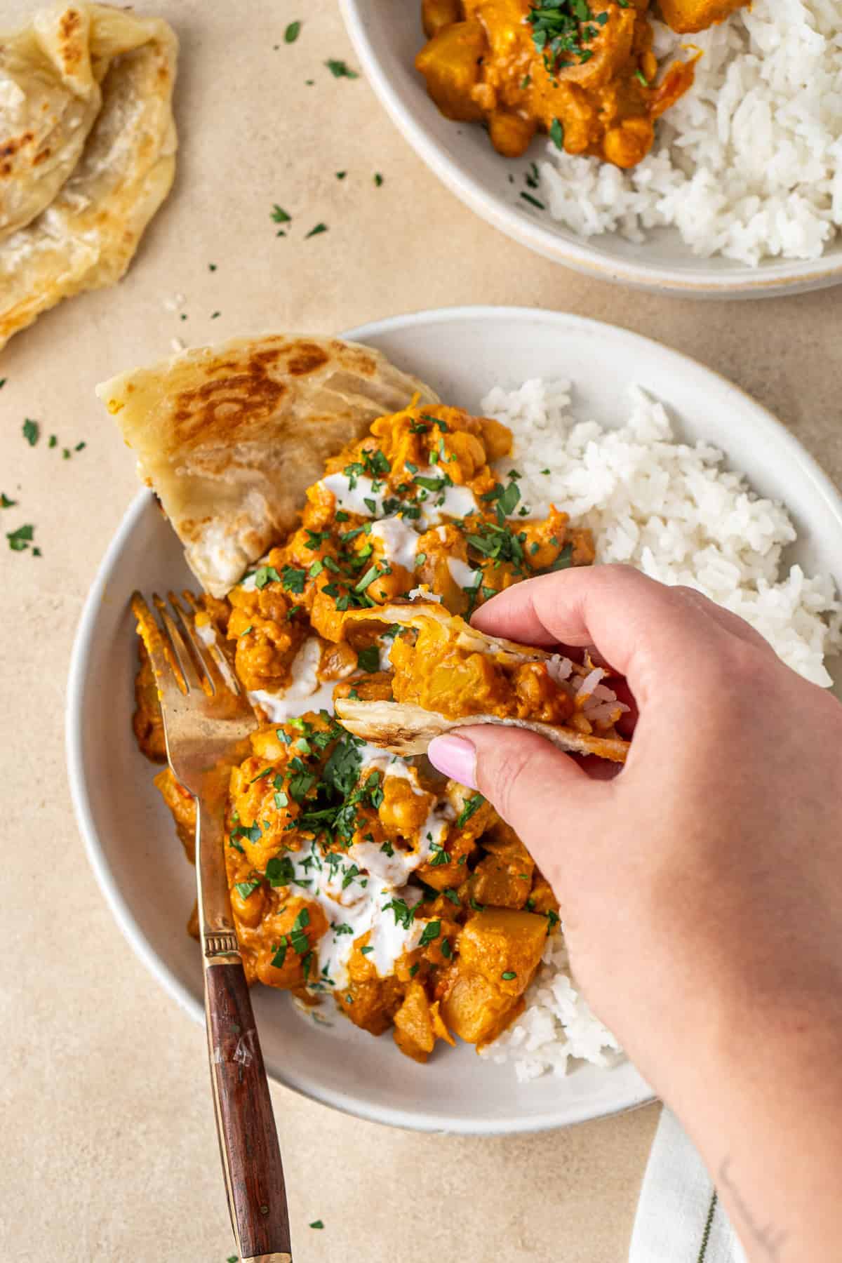 A hand taking a scoop of curry with roti.