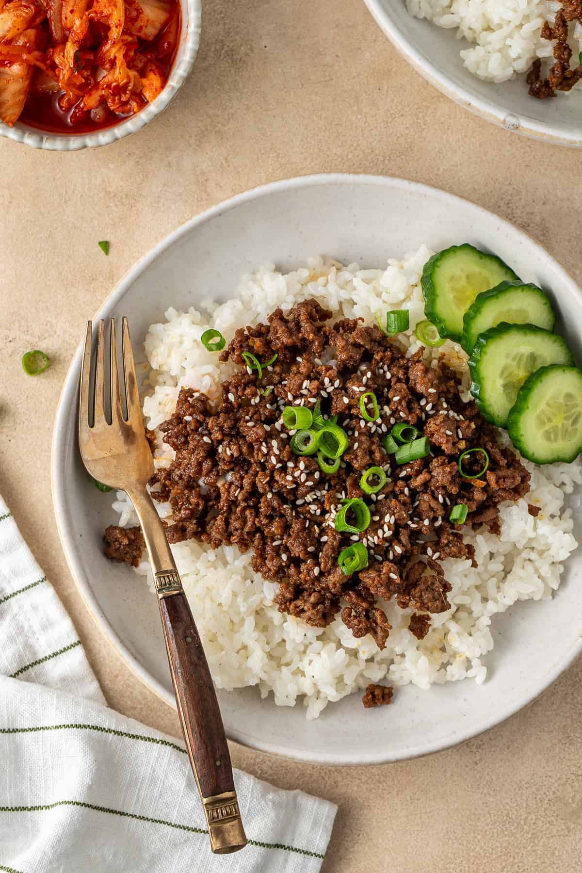 Close up of a Korean beef and rice bowl with spring onions and cucumber.