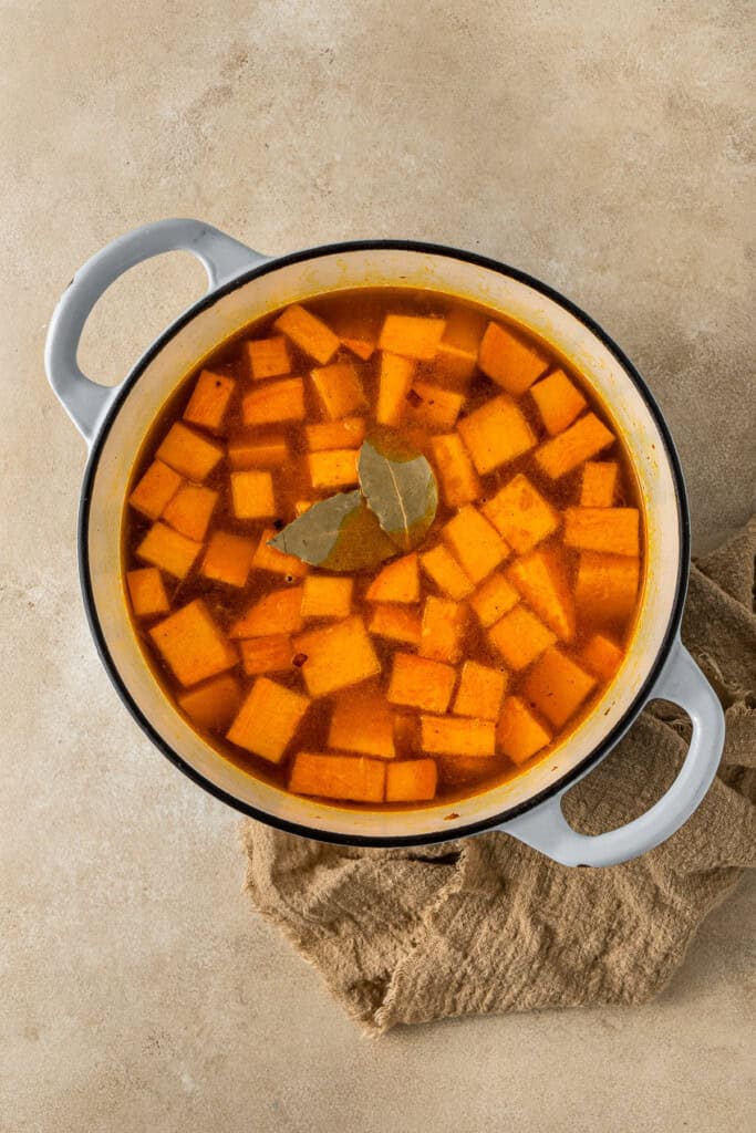 The sweet potato and bay leaves covered in water in the pot.