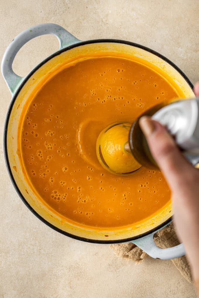 Using a stick blender to blend the soup into a smooth consistency. 