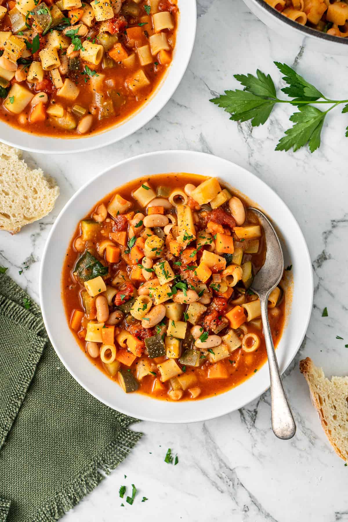 The vegetable minestrone soup served into white bowls with a spoon.