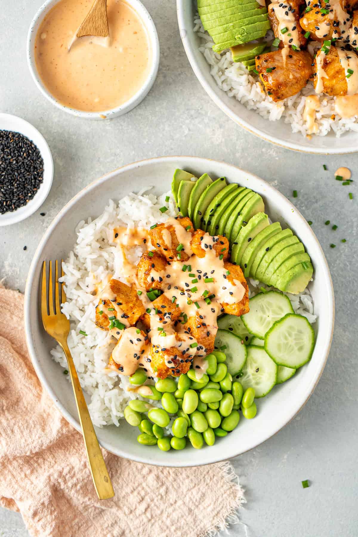 Bang bang salmon served in rice bowls with avocado, edamame and cucumber.