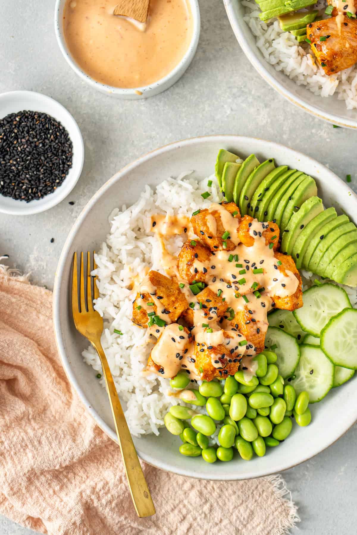 Close up of a bang bang salmon rice bowl with avocado, edamame and cucumber.