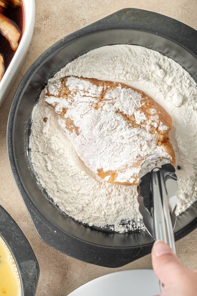 Dredging the chicken through the flour using tongs.