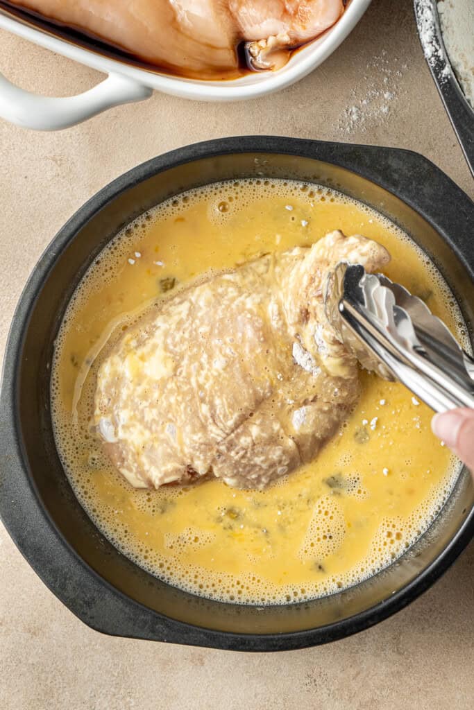Dredging the chicken through the egg wash using tongs.