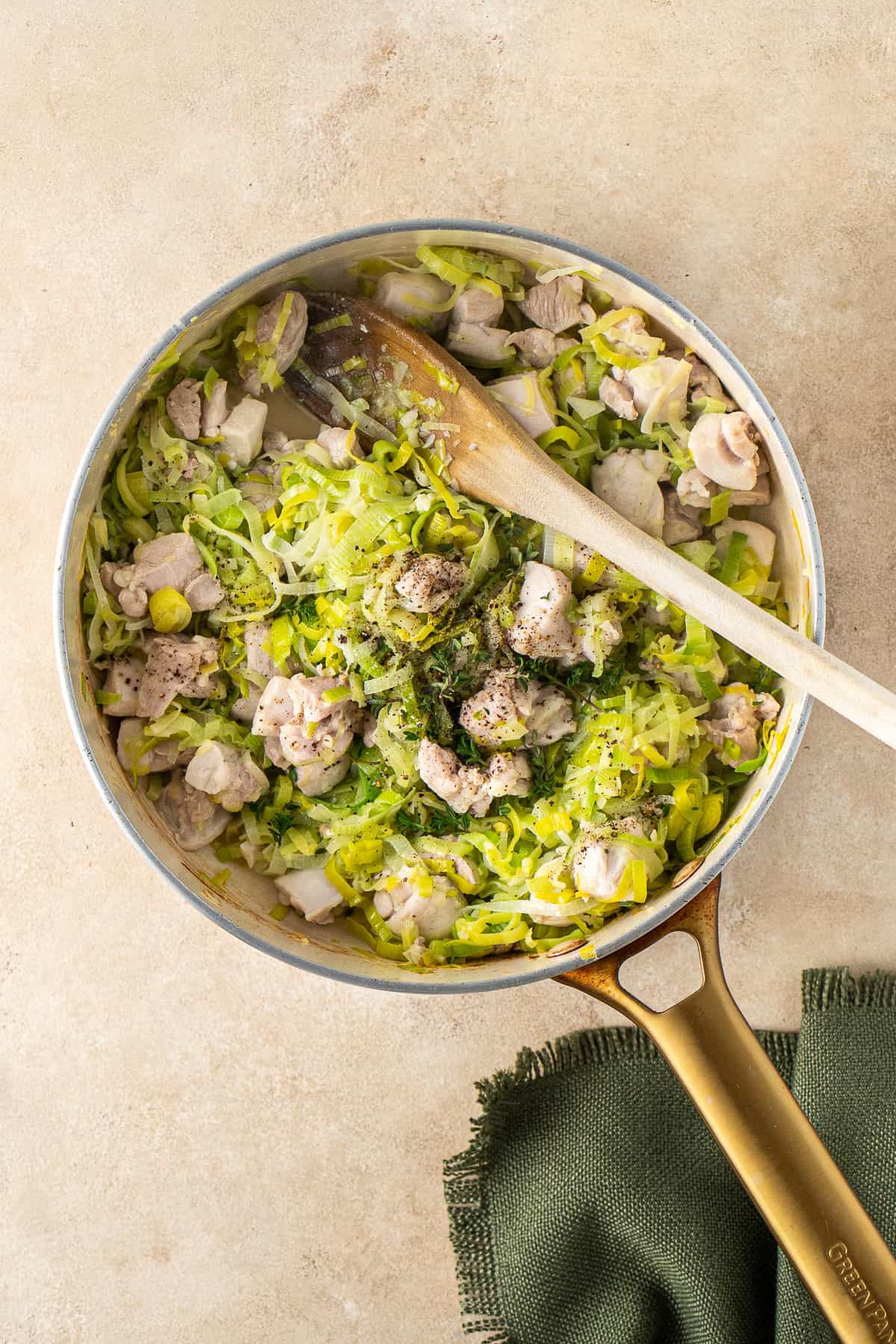 The chicken and leeks in a frying pan with a wooden spoon.