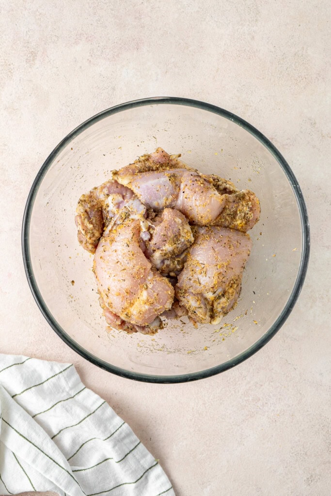 The chicken thighs in a glass bowl tossed with the seasoning.