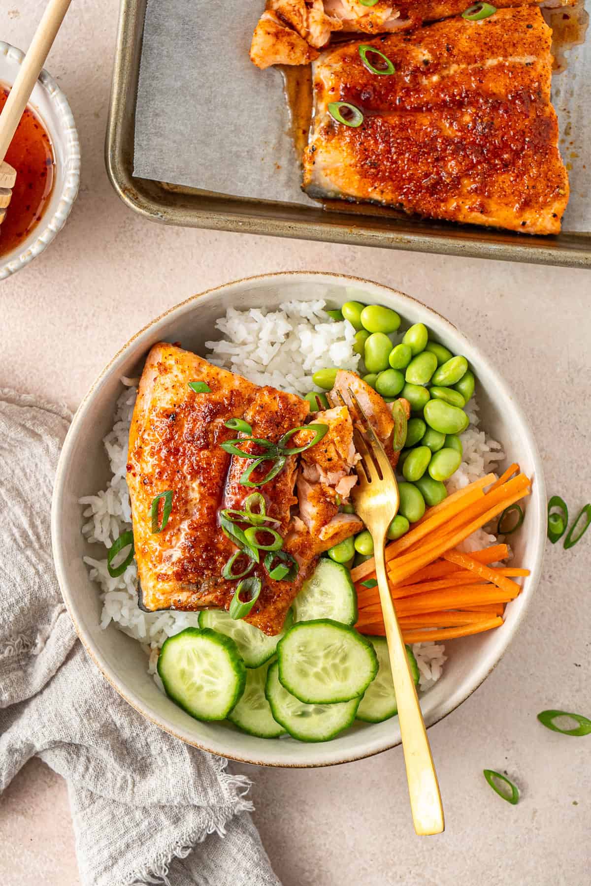 Hot honey salmon served in a bowl with rice, cucumber, edamame, carrots and spring onions.