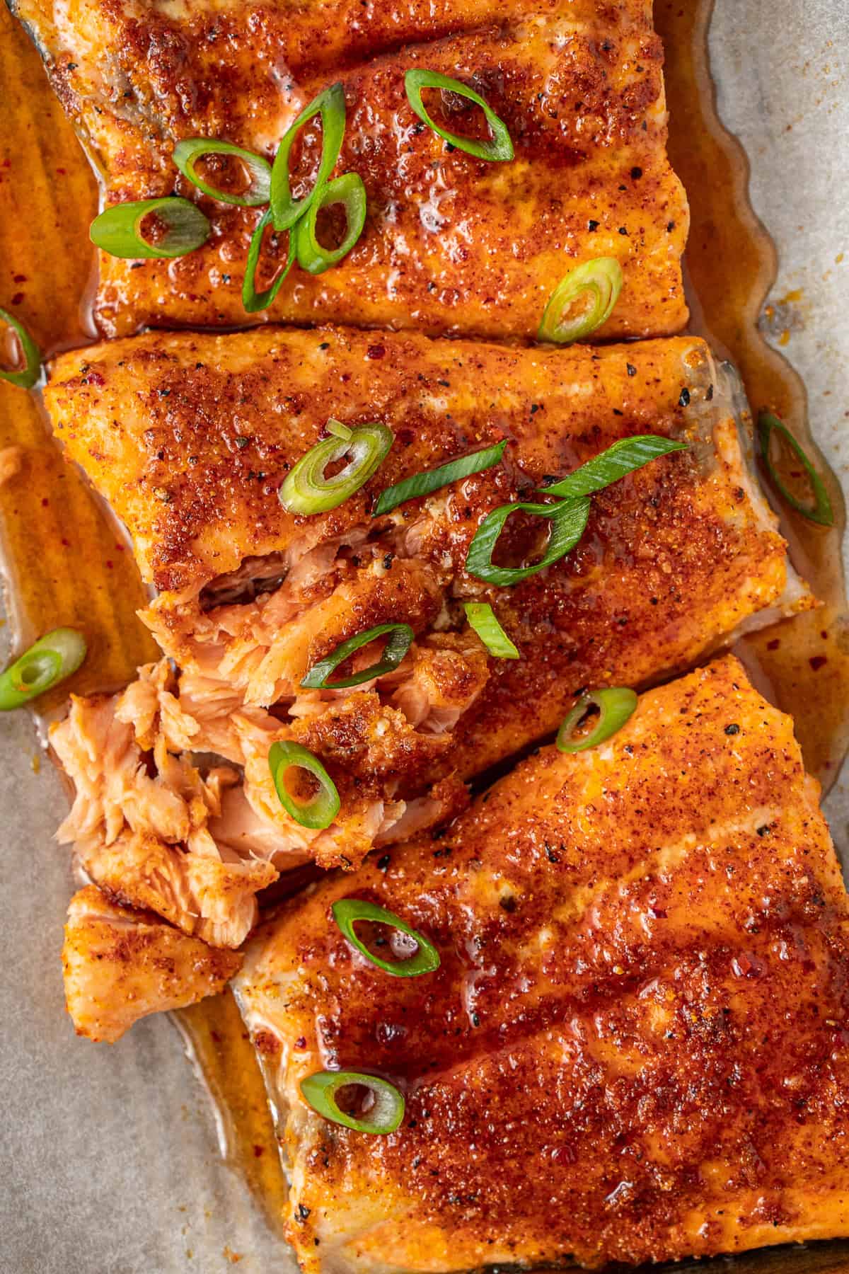 Close up of hot honey salmon on a baking tray with spring onions.