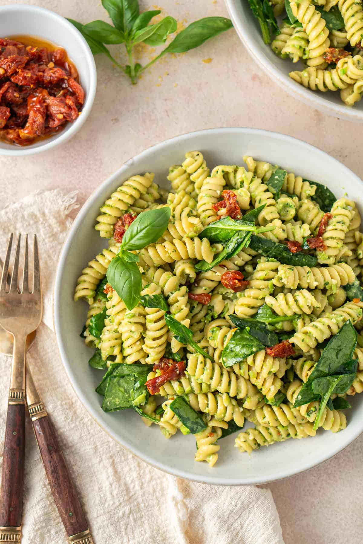 Close up of a bowl of pea pesto pasta with spinach and sundried tomatoes with forks on the side.