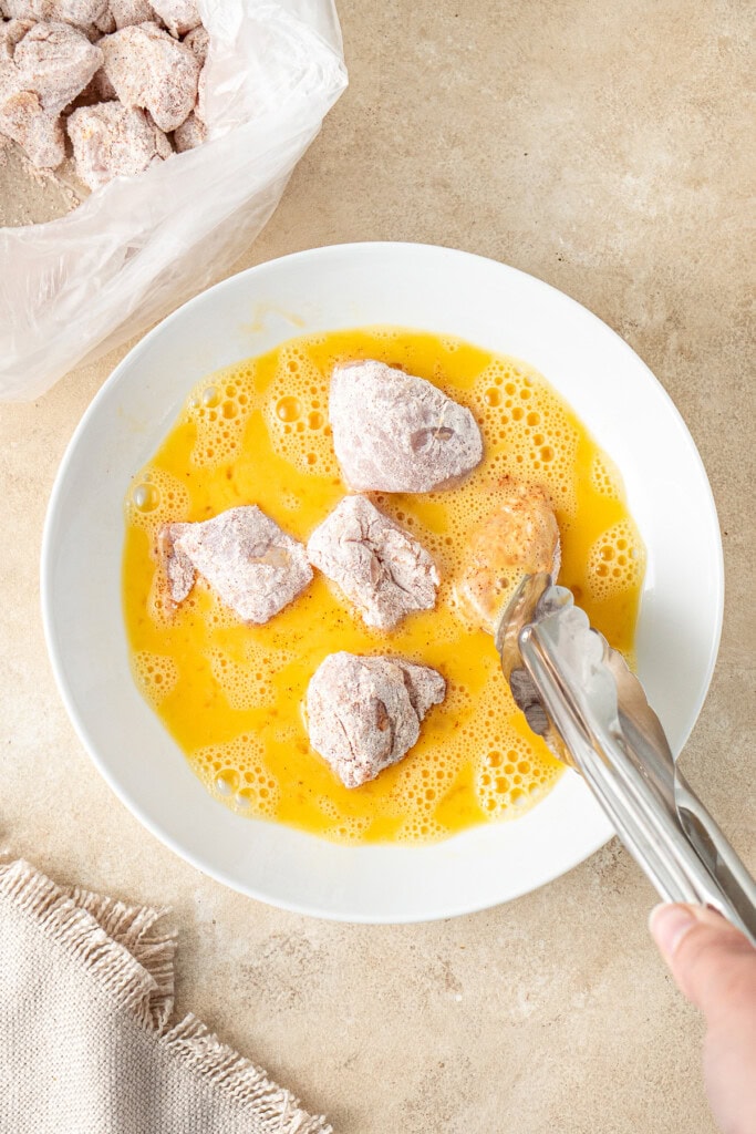 Using tongs to coat the chicken pieces in the egg.