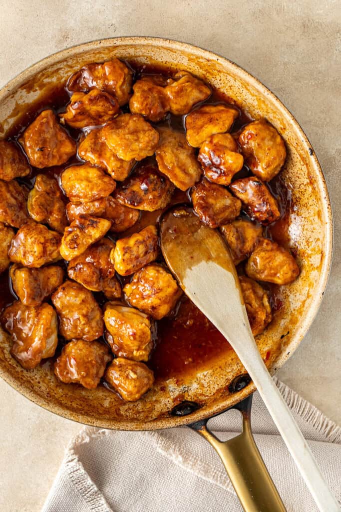 The finished sweet chilli chicken in the frying pan with a wooden spoon.